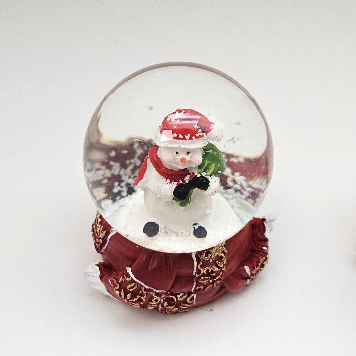 Süße Mini - Schneekugel Schneemann grüner Sack auf Sockel rot gold Winterschal B: 45mm - Schneekugelhaus