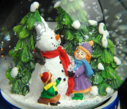 Schneekugel Kinder bauen Schneemann auf Sockel Winterlandschaft Eisläufer blau mit Spieluhr 10 cm Durchmesser - Schneekugelhaus